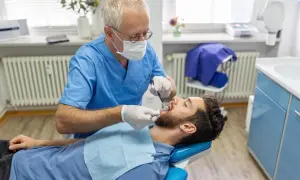 Dentysta bada pacjenta. Zastanawiasz się, ile kosztuje usunięcie ósemki na NFZ? Wizyta u stomatologa to pierwszy krok.