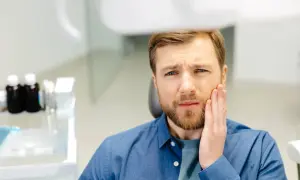 Mężczyzna z bólem zęba, zastanawia się, jak długo boli ząb po zatruciu.