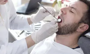Dentysta bada zęby pacjenta. Rozważasz pokrycie recesji dziąsła NFZ? Wizyta u stomatologa to pierwszy krok.