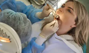 Kobieta przechodzi leczenie stomatologiczne NFZ. Dentysta w rękawiczkach bada jej zęby.