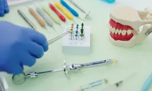 Rękawiczka w niebieskiej rękawiczce trzyma narzędzie do czyszczenia protezy zębowej sodą. Obok model szczęki i narzędzia dentystyczne.
