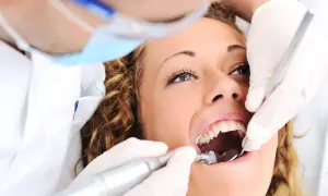Kobieta u dentysty, zastanawia się ile kosztuje plomba prywatnie. Dentysta w rękawiczkach używa wiertła i lusterka.