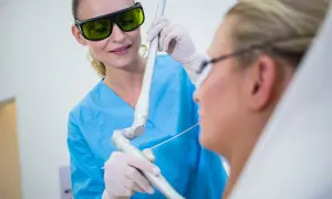 Lekarka w okularach ochronnych wykonuje laserowe usuwanie zmian w jamie ustnej pacjentki.