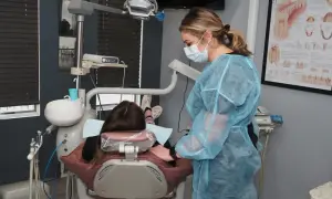 Dentystka w fartuchu przygotowuje się do skalingu i piaskowania NFZ. Pacjentka leży w fotelu.