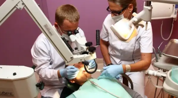 Dentysta i asystentka pracują przy pacjencie pod mikroskopem stomatologicznym.