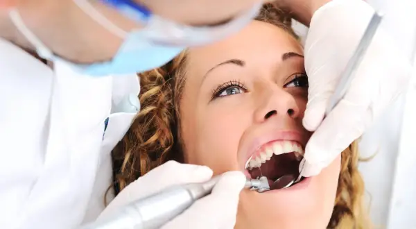 Kobieta u dentysty, zastanawia się ile kosztuje plomba prywatnie. Dentysta w rękawiczkach używa wiertła i lusterka.