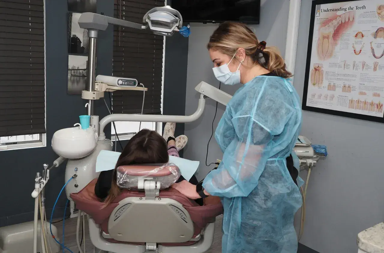 Dentystka w fartuchu przygotowuje się do skalingu i piaskowania NFZ. Pacjentka leży w fotelu.