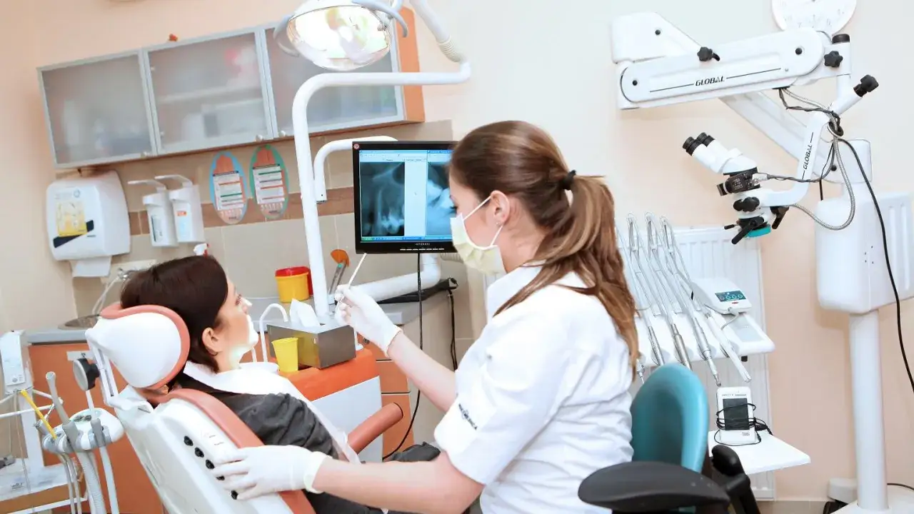 Dentystka w masce analizuje zdjęcie rentgenowskie zębów pacjentki, przygotowując się do zabiegu czyszczenia zębów na NFZ.
