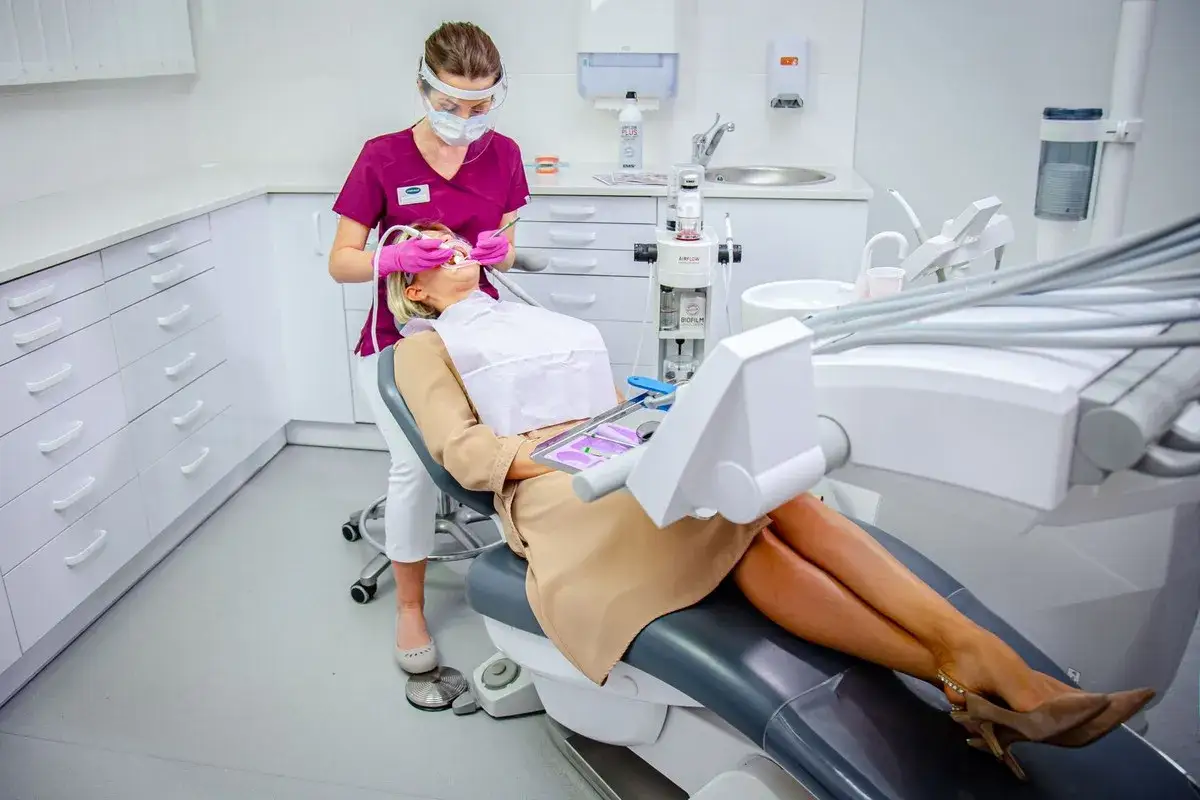 Stomatologia dla niepełnosprawnych NFZ: dentystka w masce i przyłbicy bada pacjentkę w gabinecie.