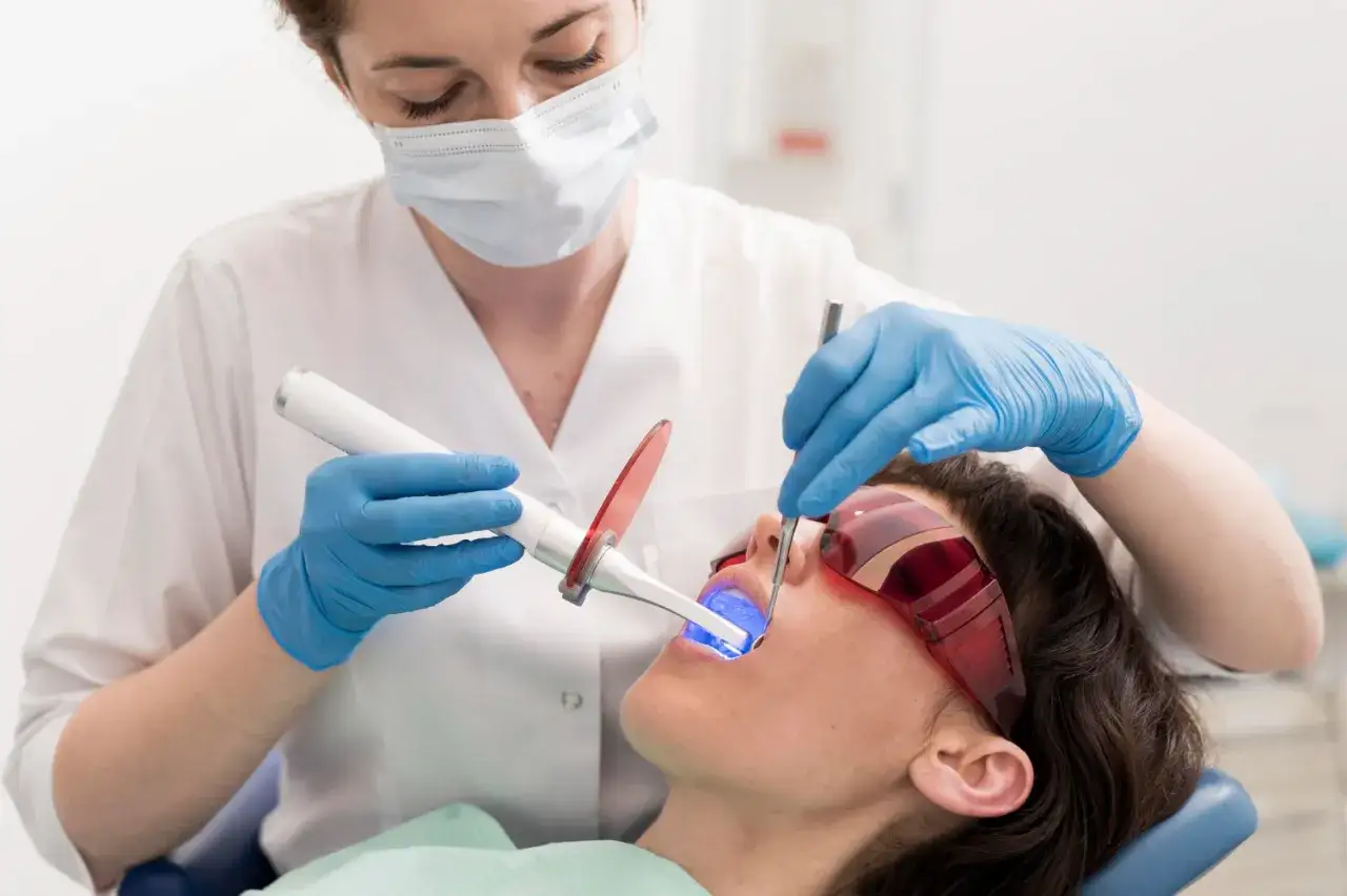 Dentystka wykonuje laserowe usuwanie zmian w jamie ustnej u pacjentki w okularach ochronnych.