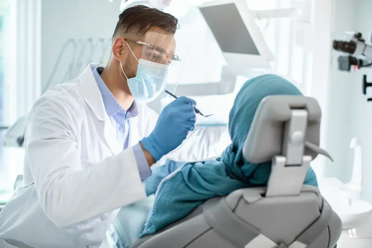 Dentysta w masce i rękawiczkach bada pacjentkę. Dostępna stomatologia dla niepełnosprawnych NFZ.