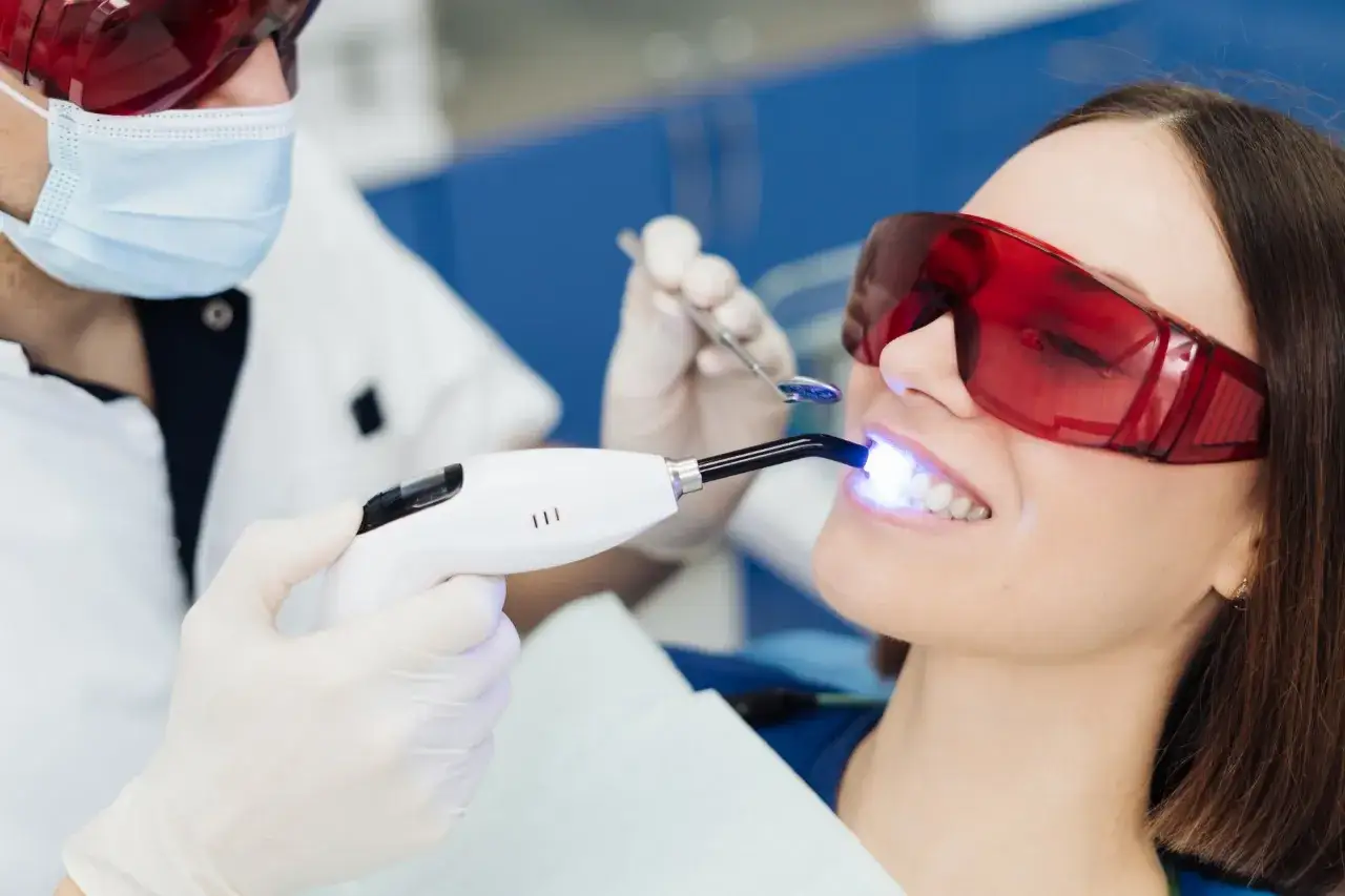 Dentysta wykonuje laserowe usuwanie zmian w jamie ustnej u pacjentki w okularach ochronnych.