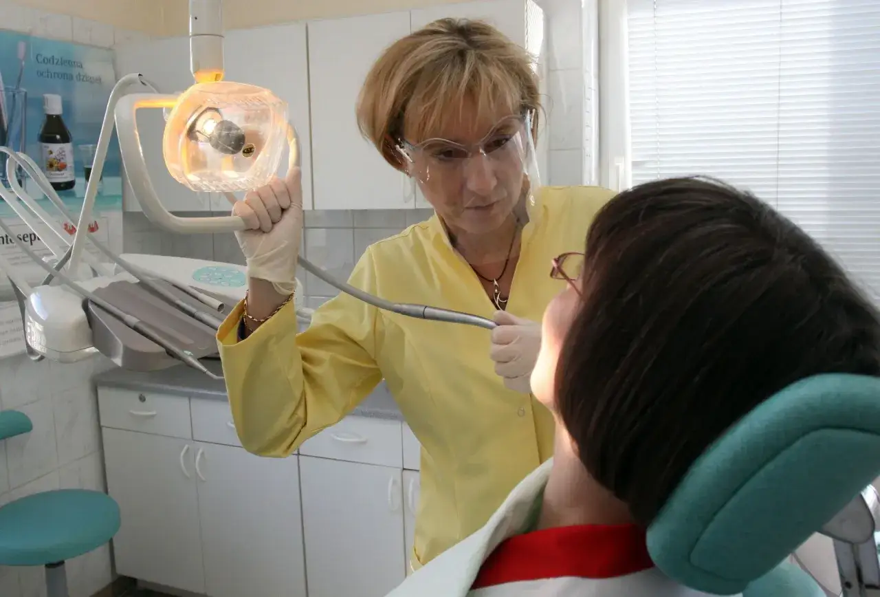 Dentystka w żółtej bluzce i goglach pomaga pacjentowi, który cierpi z bólu zęba w weekend.