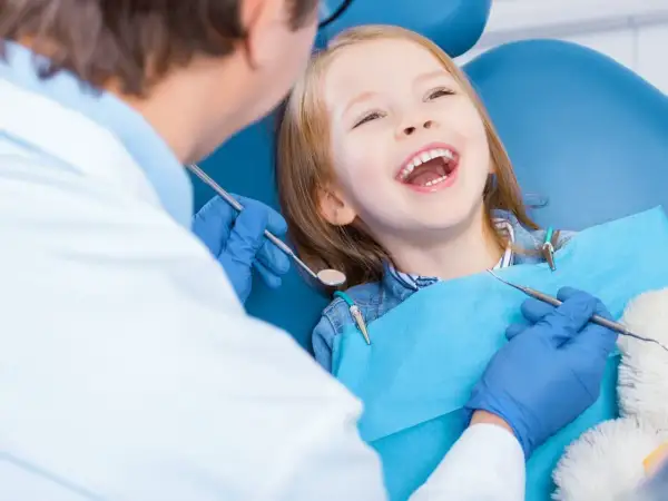 Uśmiechnięta dziewczynka u dentysty, która ma krzywy zgryz. Lekarz bada jej zęby.